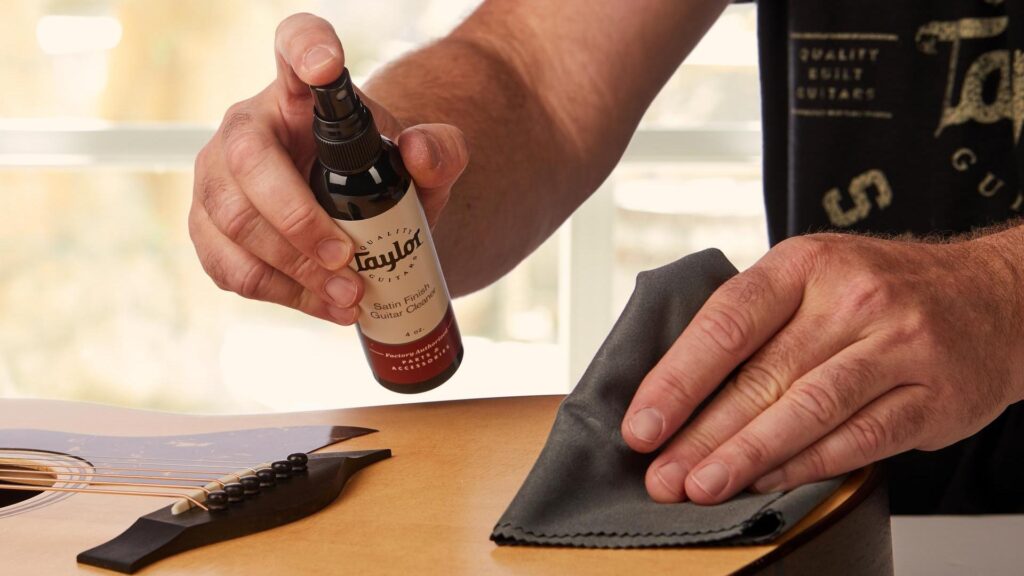 Image of a person spraying Taylor guitar polish on an acoustic guitar and wiping the guitar with a microfiber cloth