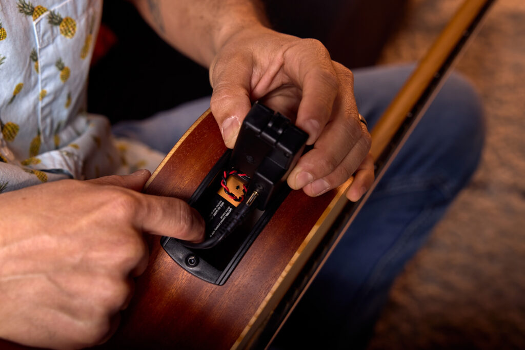 Image of guitarist opening ES-B preamp unit on acoustic guitar to expose 9-volt battery